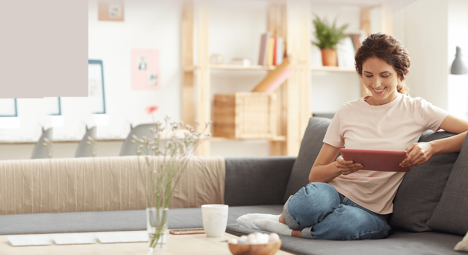 Woman sitting on a couch at home, smiling while using a tablet.