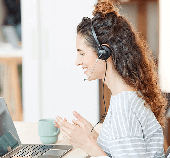 A woman with a headset sitting at a desk with a laptop.